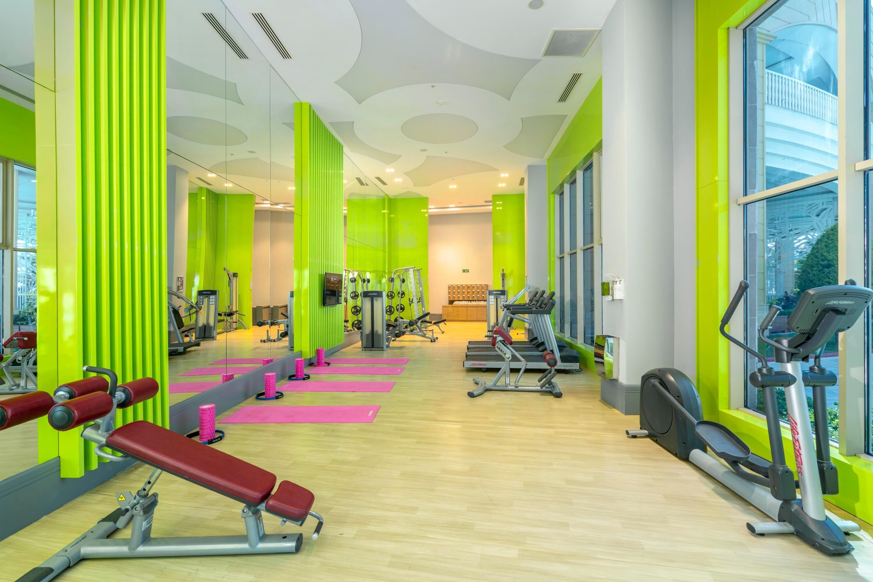 A gym with exercise equipment, large windows, and bright green walls.
