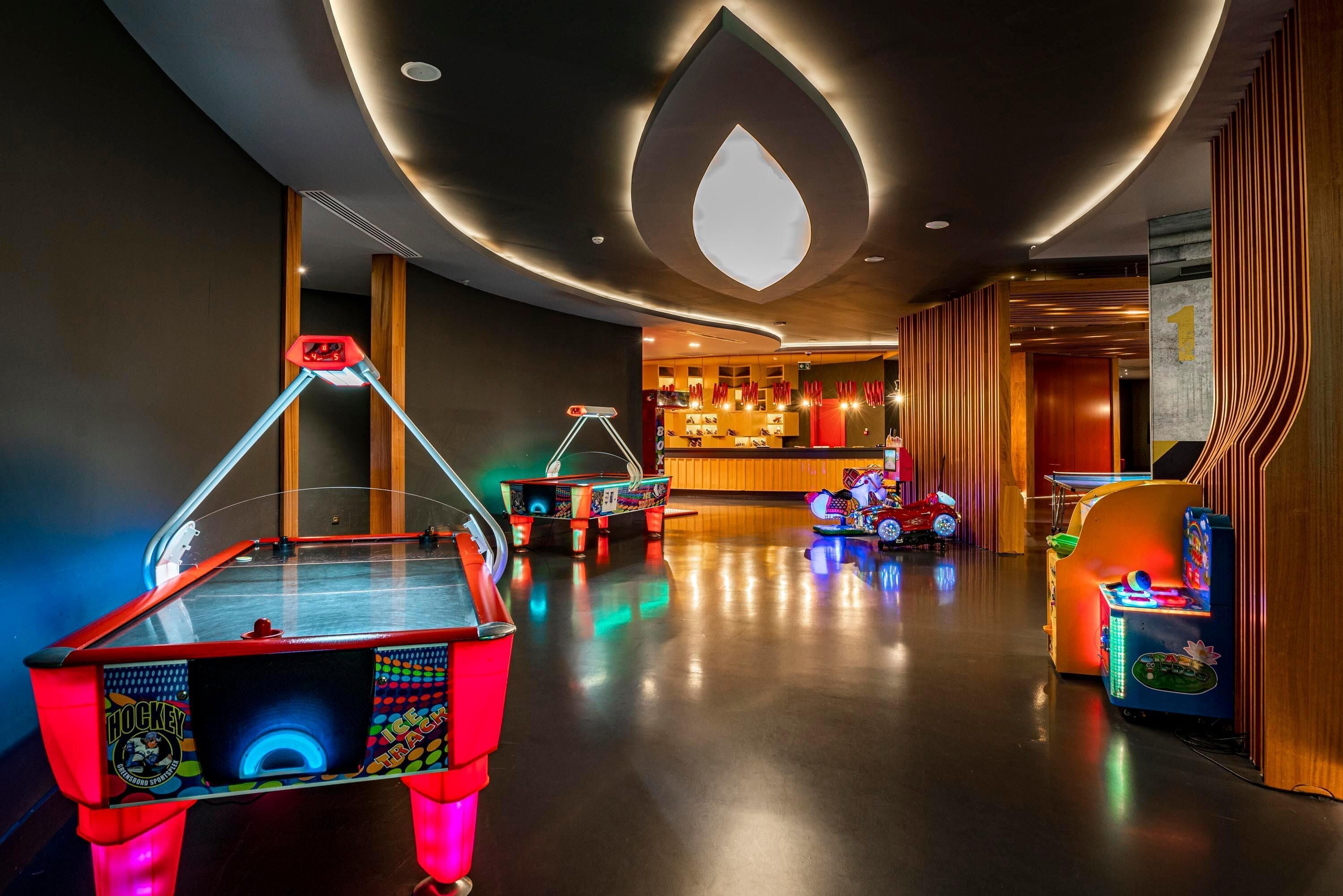 A modern indoor space with a foosball table, arcade games, and a bar area.