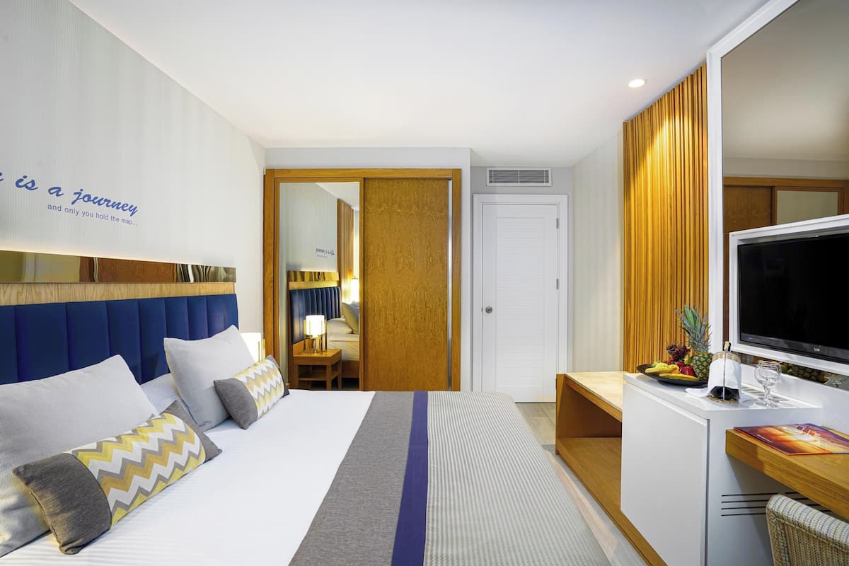 Een hotelkamer met een bed, een televisie, een bureau met een computer en een deur naar een andere kamer.