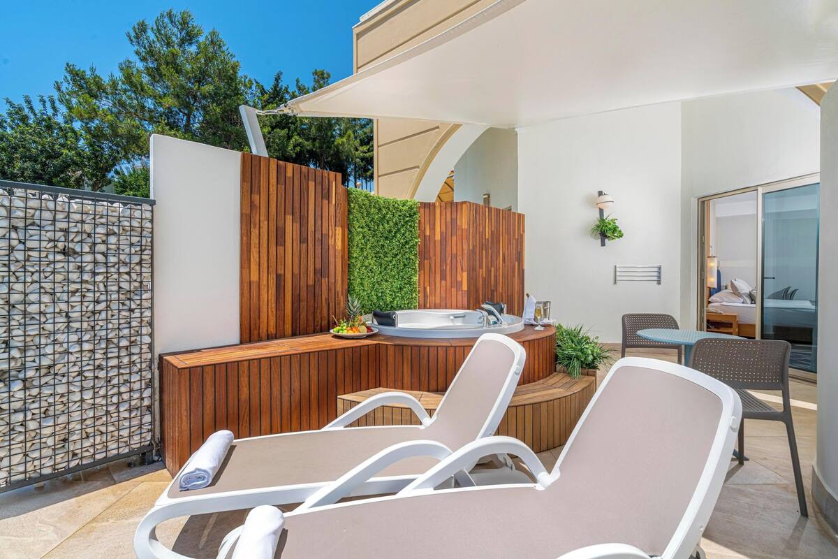 Een moderne terrasruimte buiten met een jacuzzi, houten lambrisering en een zithoek met loungestoelen.