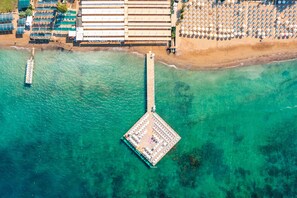 Vista aérea de un hotel frente al mar, con un muelle, sombrillas de playa y una zona de piscina.