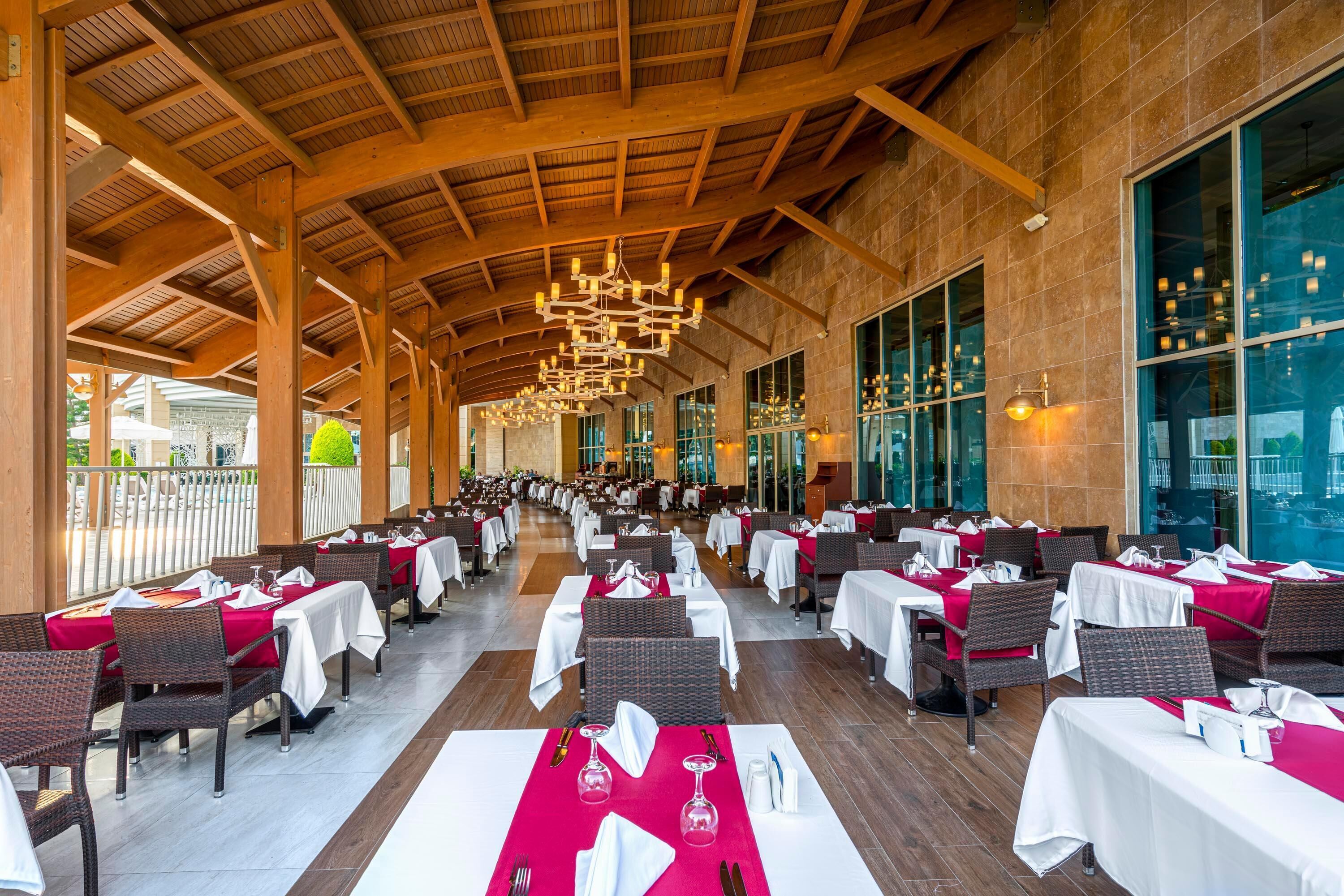 Un vaste espace de restauration intérieur, doté de hauts plafonds et de grandes fenêtres, et comprenant de nombreuses tables dressées pour le repas.
