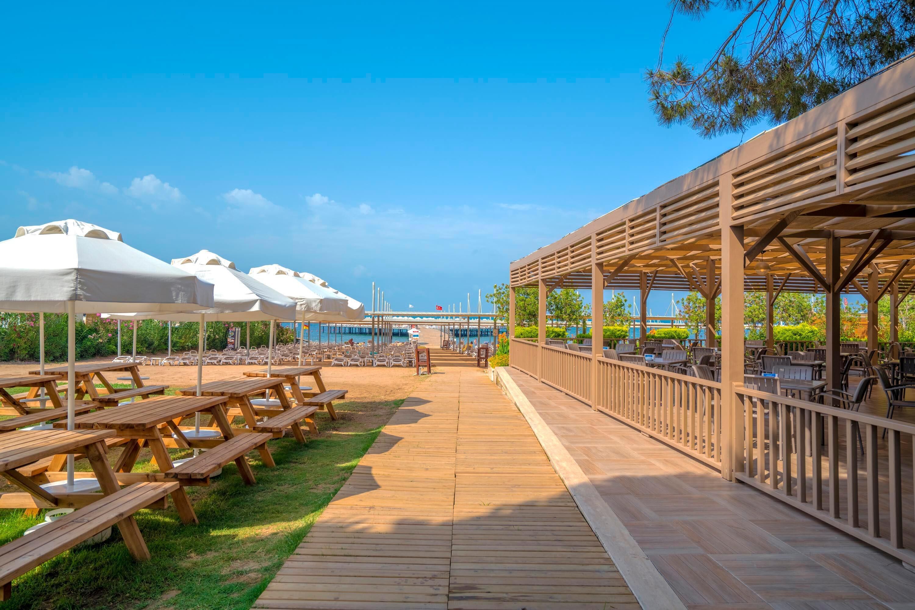 Una terraza de madera con mesas de picnic y sombrillas, con vistas a una masa de agua.