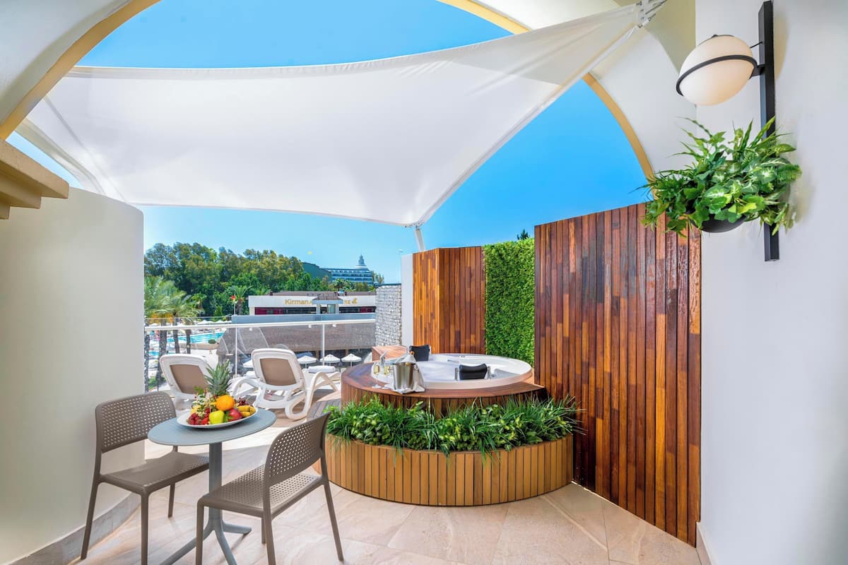 Een terras op het dak met een ronde tafel, stoelen, een jacuzzi en een houten plantenbak met groen.