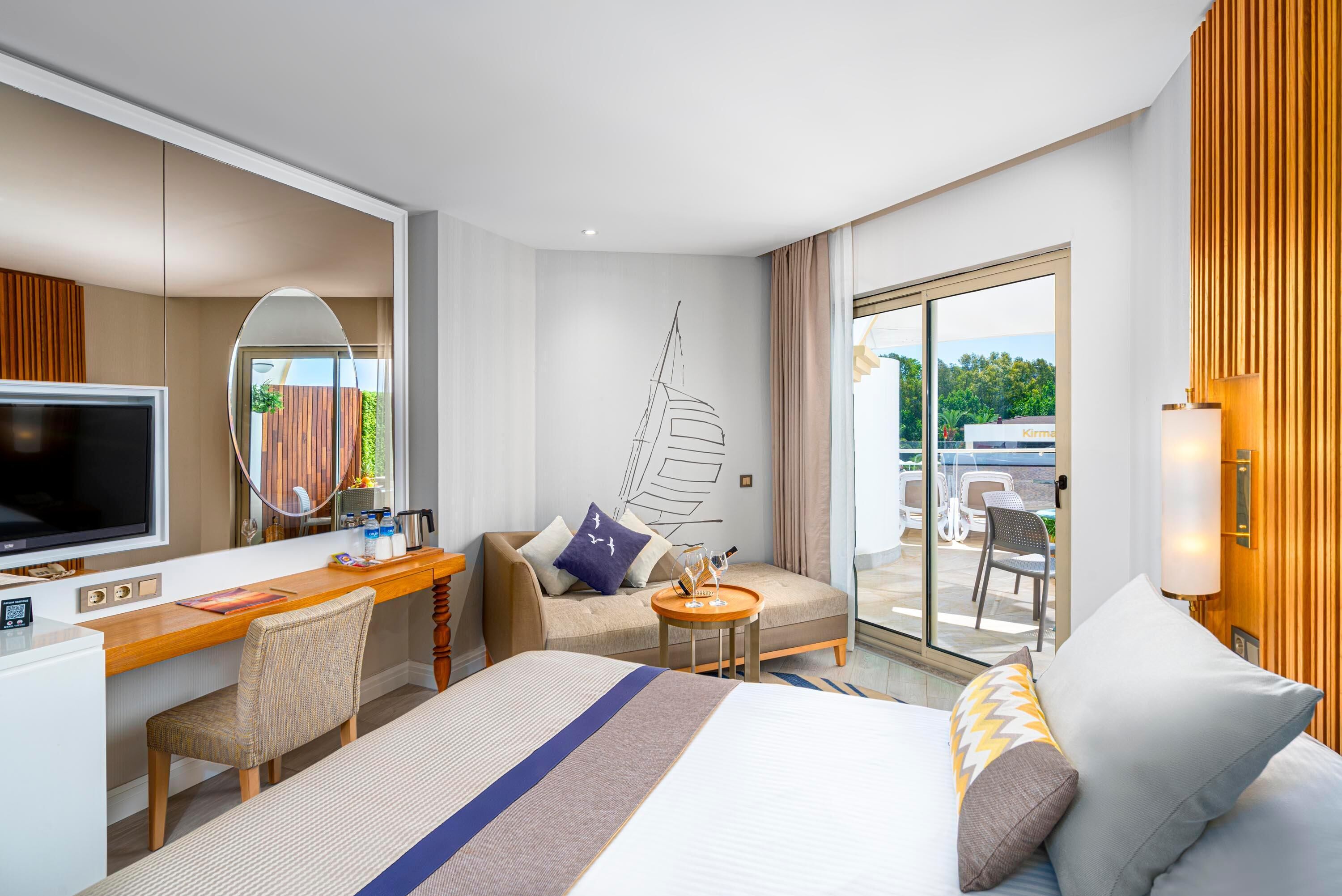 Une chambre d’hôtel équipée d’un lit, d’un bureau, d’une chaise, d’une télévision et d’un balcon avec du mobilier d’extérieur.