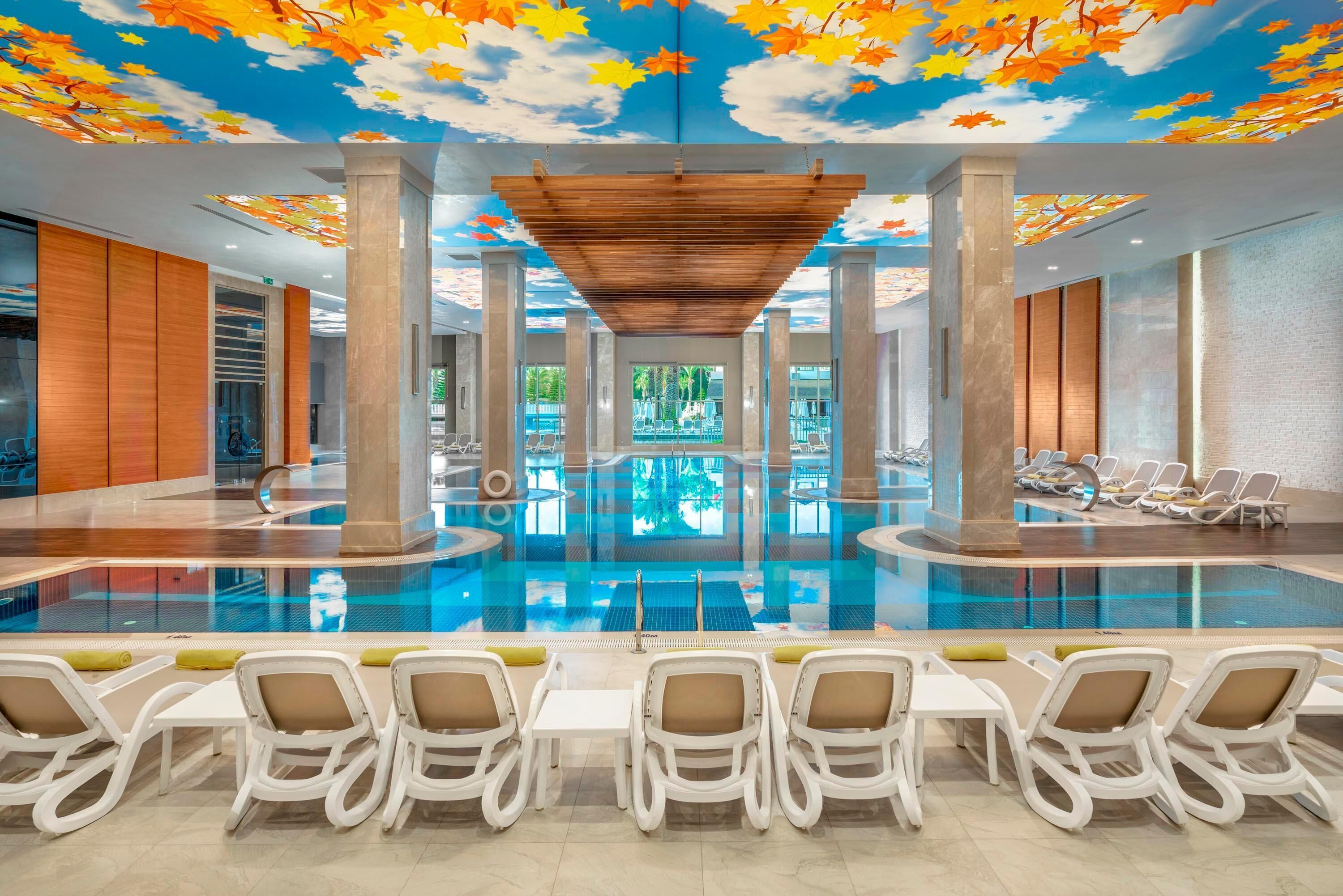 Una piscina interior con sillones de descanso, estructura de techo de madera y vistas al exterior.