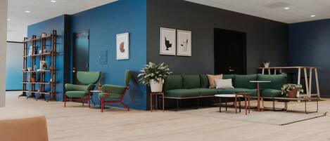 A modern living room with a blue accent wall, green sofas, a wooden coffee table, and a bookshelf.