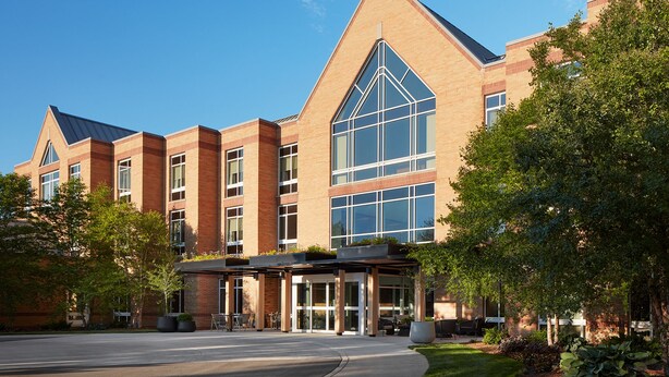 A modern building with a prominent glass facade, a brick exterior, and a landscaped entrance area with seating.