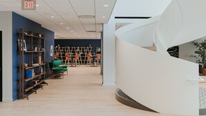 A modern interior with a spiral staircase, wooden shelves, and green chairs.