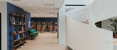 A modern interior with a spiral staircase, wooden shelves, and green chairs.