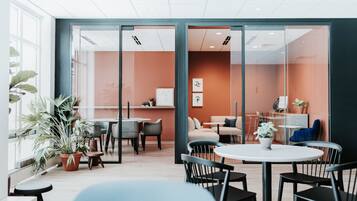 Un ufficio moderno con pareti divisorie in vetro, una sala riunioni con tavoli e sedie, e un'area relax con divani e un tavolino.