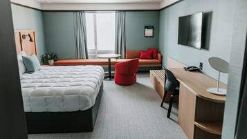 Una habitación de hotel moderna con cama, escritorio, silla, sofá, televisor y ventana con cortinas.