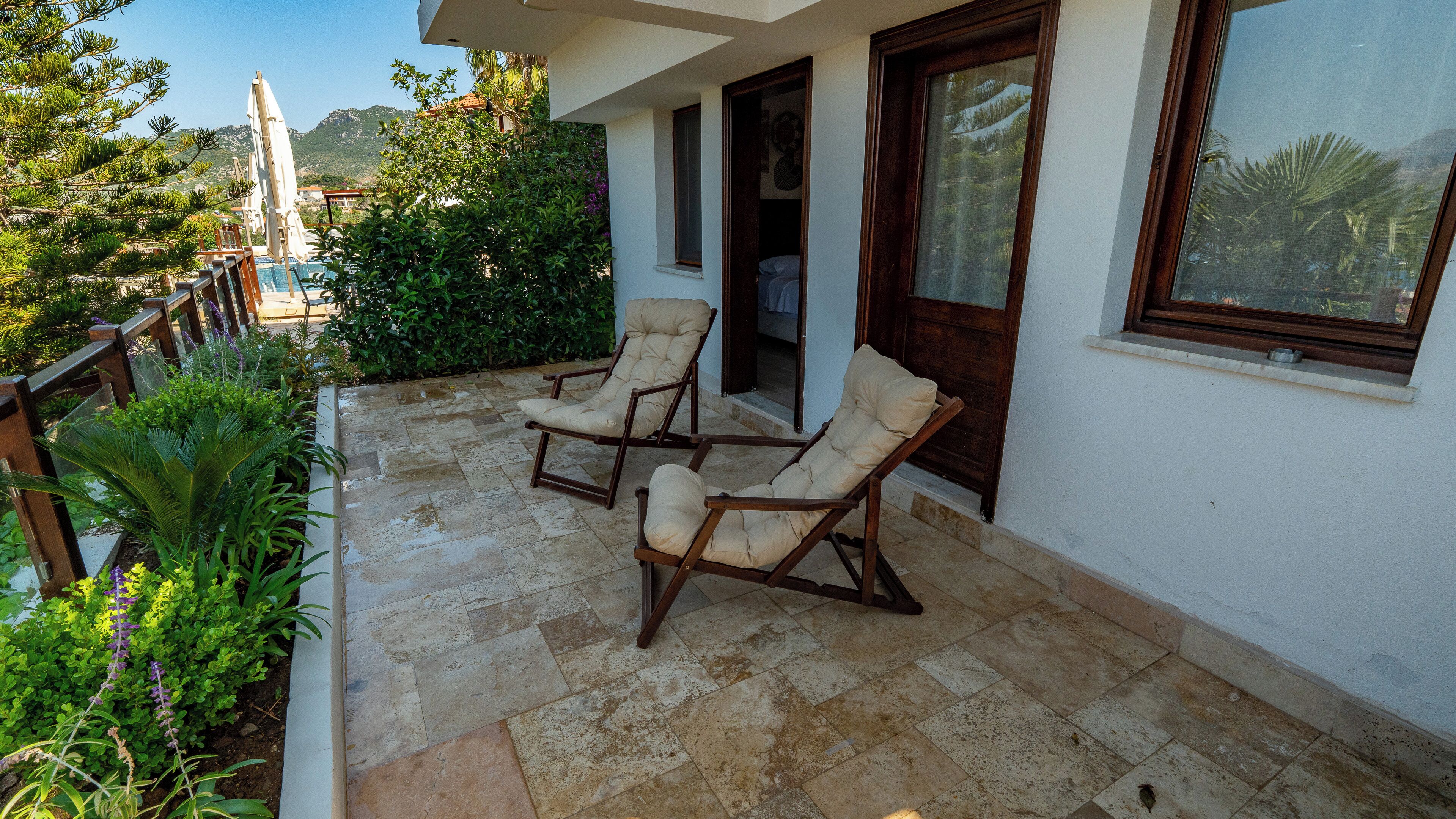 A balcony with two lounge chairs, a stone tiled floor, and a view of the surrounding greenery and mountains.