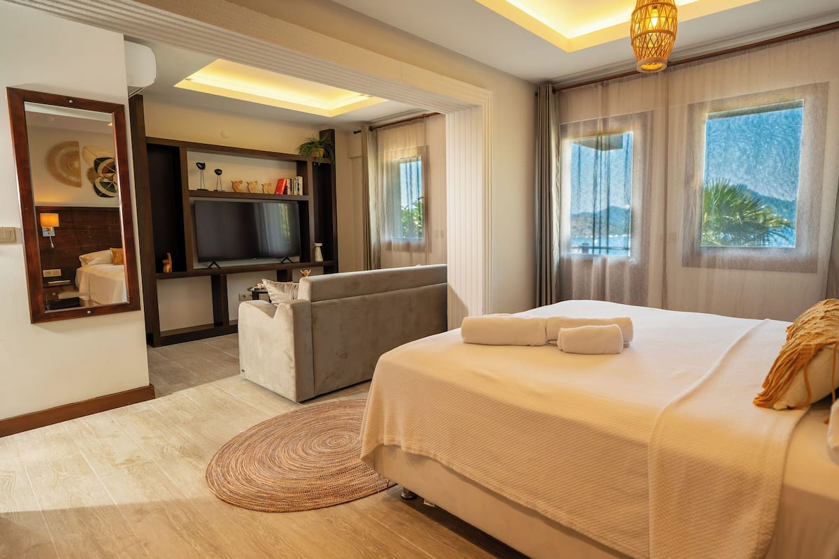 A hotel room with a bed, a sofa, a TV, a window with a view, and a ceiling light.