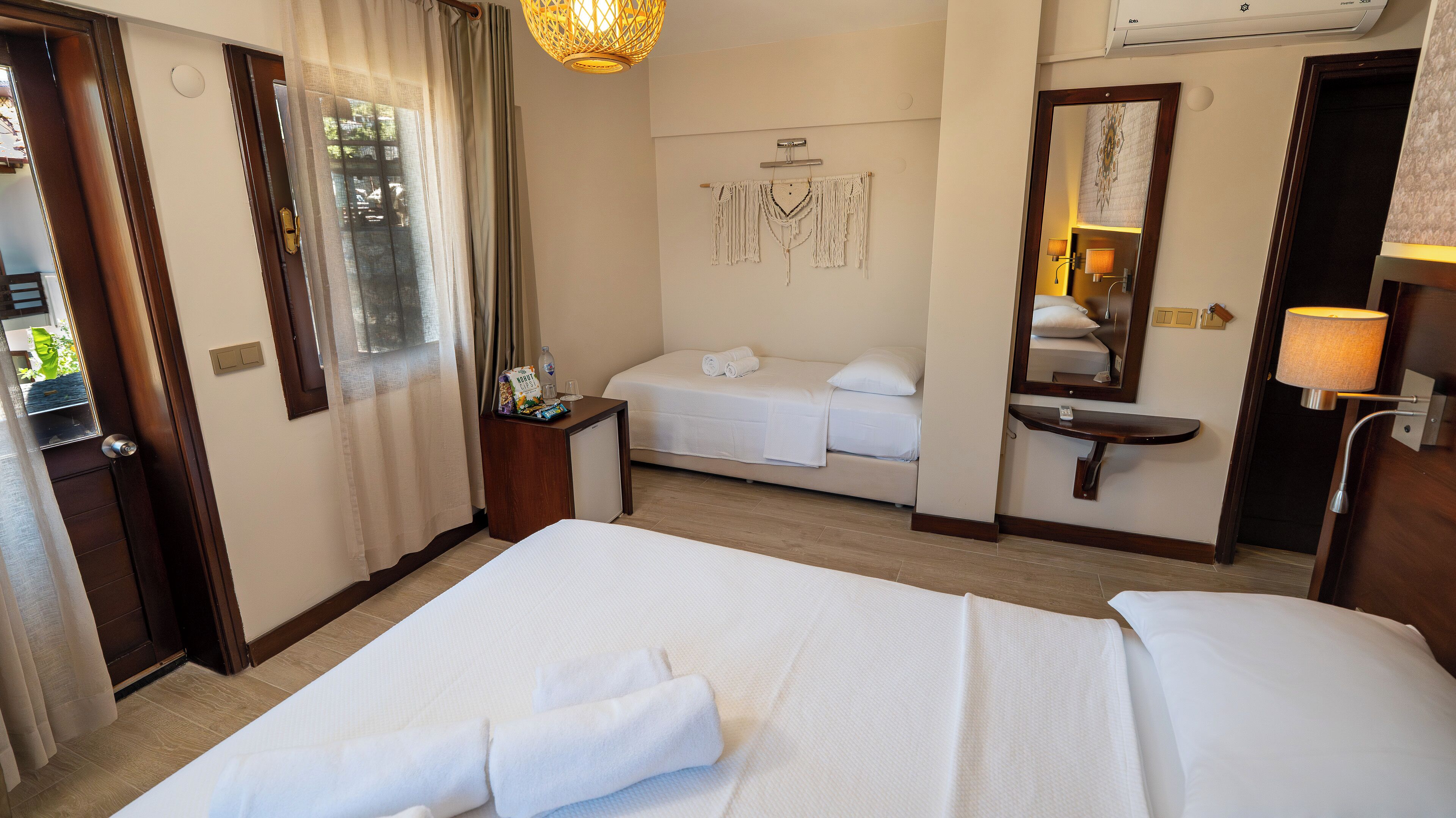 Une chambre d’hôtel comprenant un lit, une table de chevet, un miroir, un climatiseur fixé au mur et une fenêtre avec des rideaux.