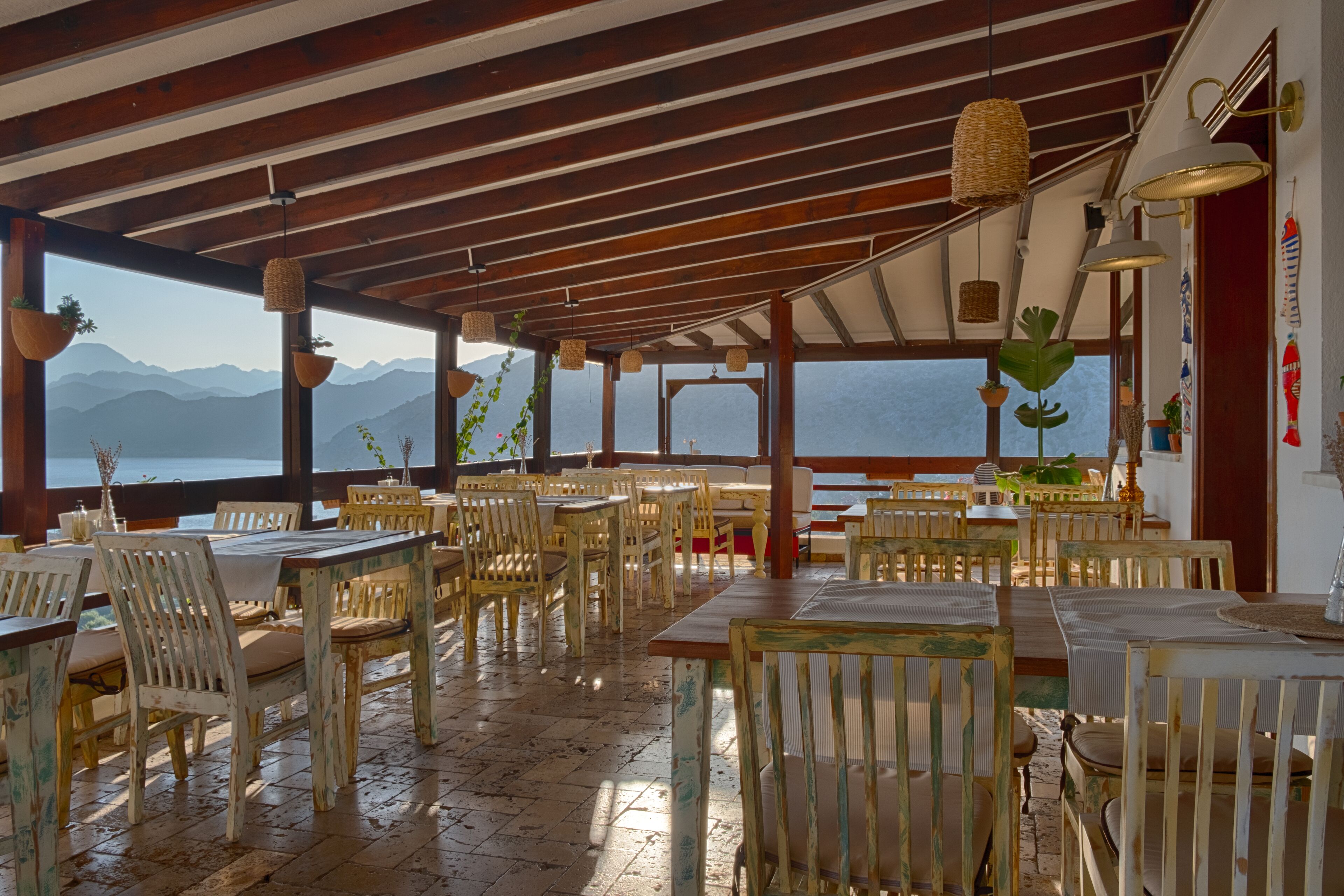 A restaurant with wooden tables and chairs, hanging baskets with plants, and a view of the mountains.