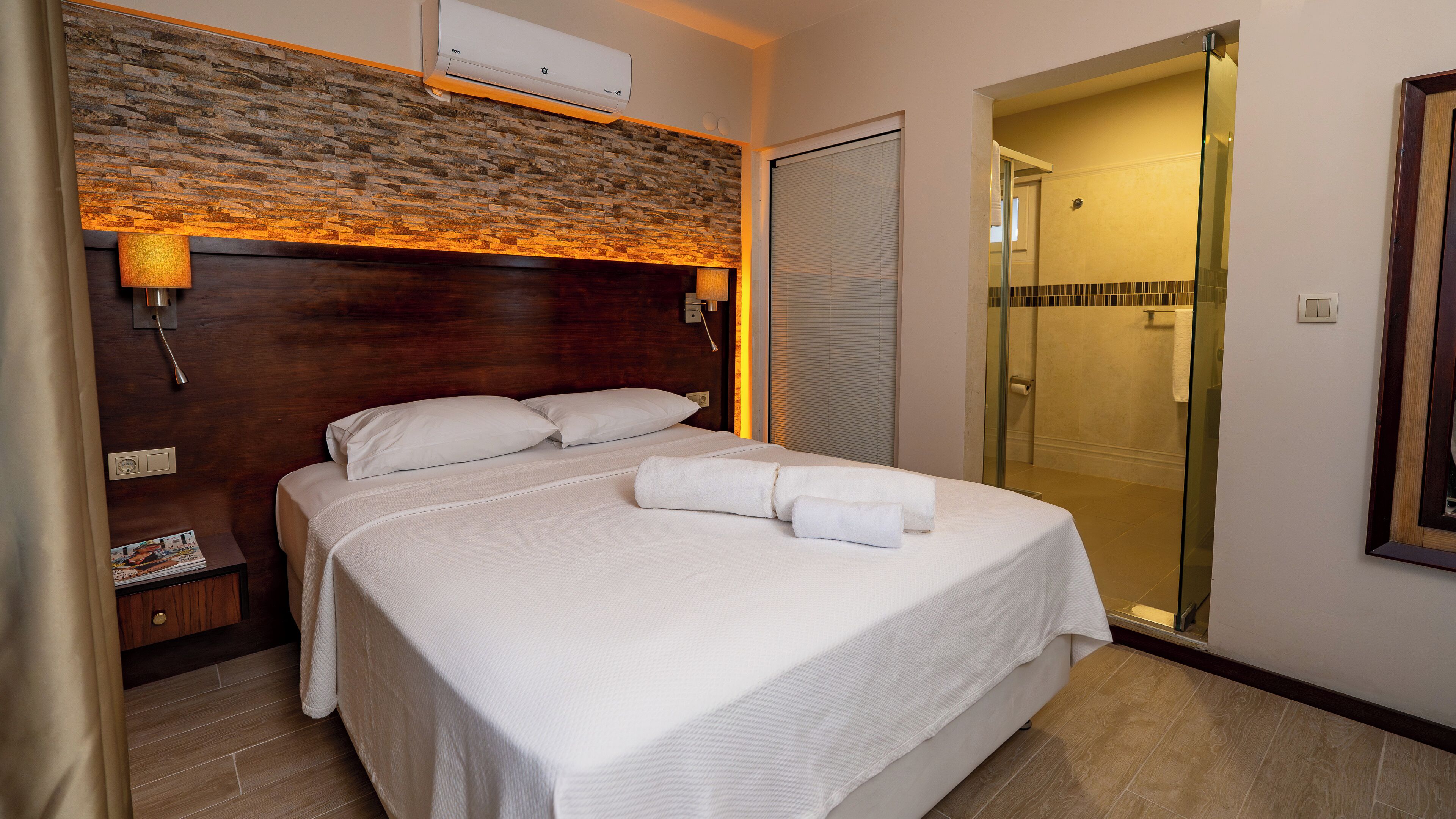 Camera d'albergo con un letto, un comodino, una lampada, un condizionatore d'aria a muro e uno spazio doccia.