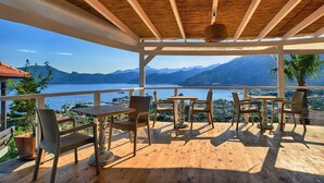 A wooden deck with tables and chairs overlooking a lake and mountains. - Les Terrasses De Selimiye (Marmaris)
