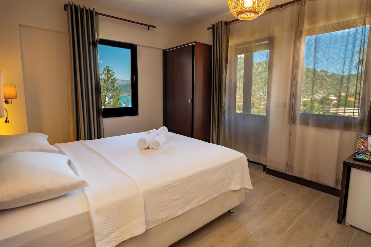 A hotel room with a bed, a nightstand, a lamp, a window with a view, and a door.