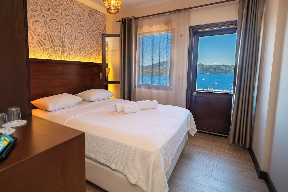 A hotel room with a bed, a nightstand with toiletries, a view of the sea, and a patterned wall.