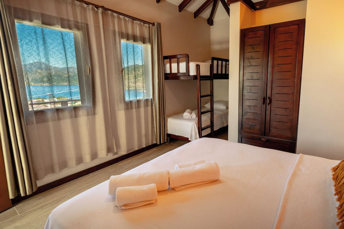 A hotel room with a bed, a window with curtains, a wooden wardrobe, and a view of the sea.