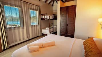 Habitación de hotel con cama, ventana con cortinas, armario de madera y vista al mar.