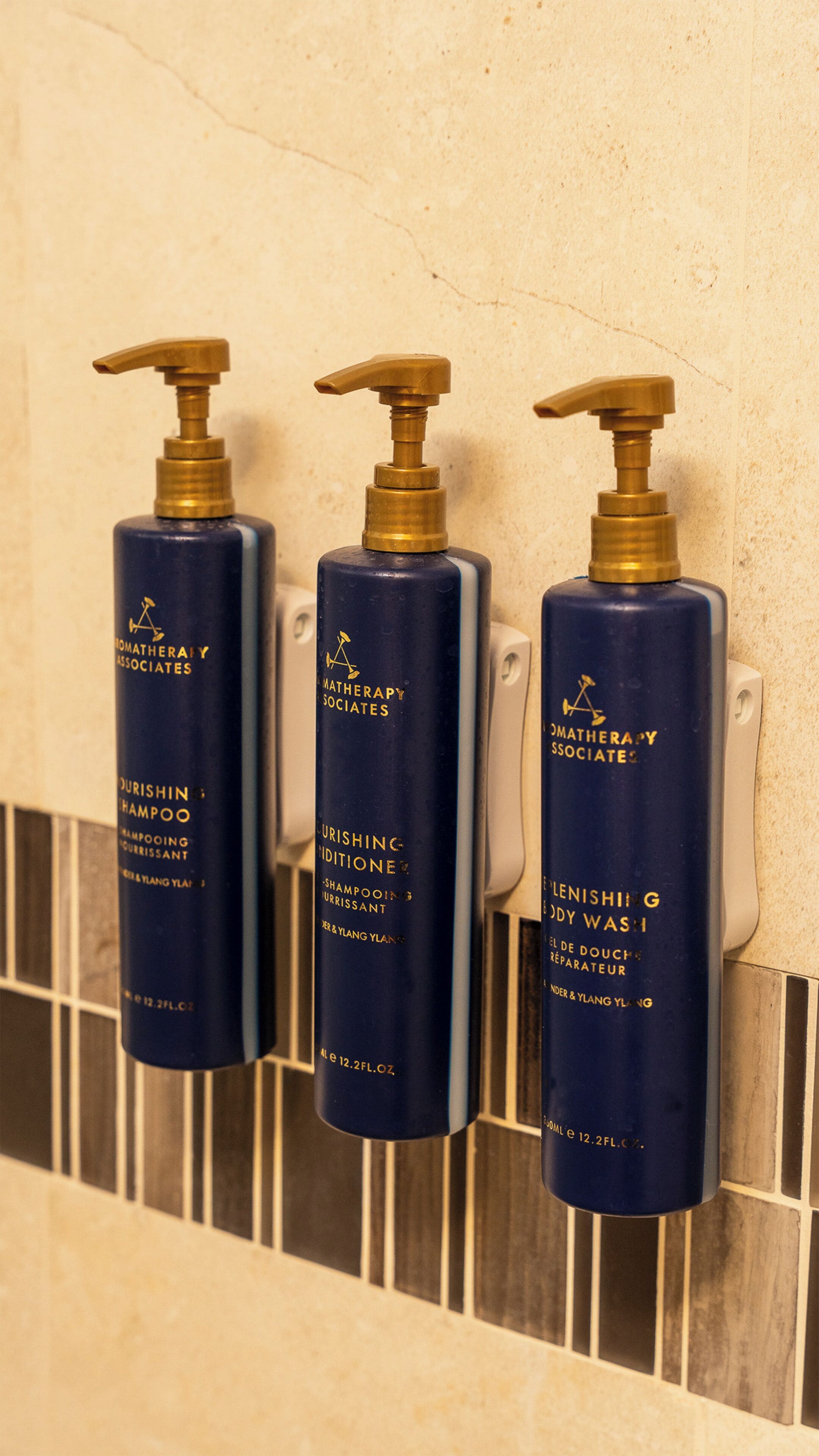 Three bottles of hair care products mounted on a tiled wall.