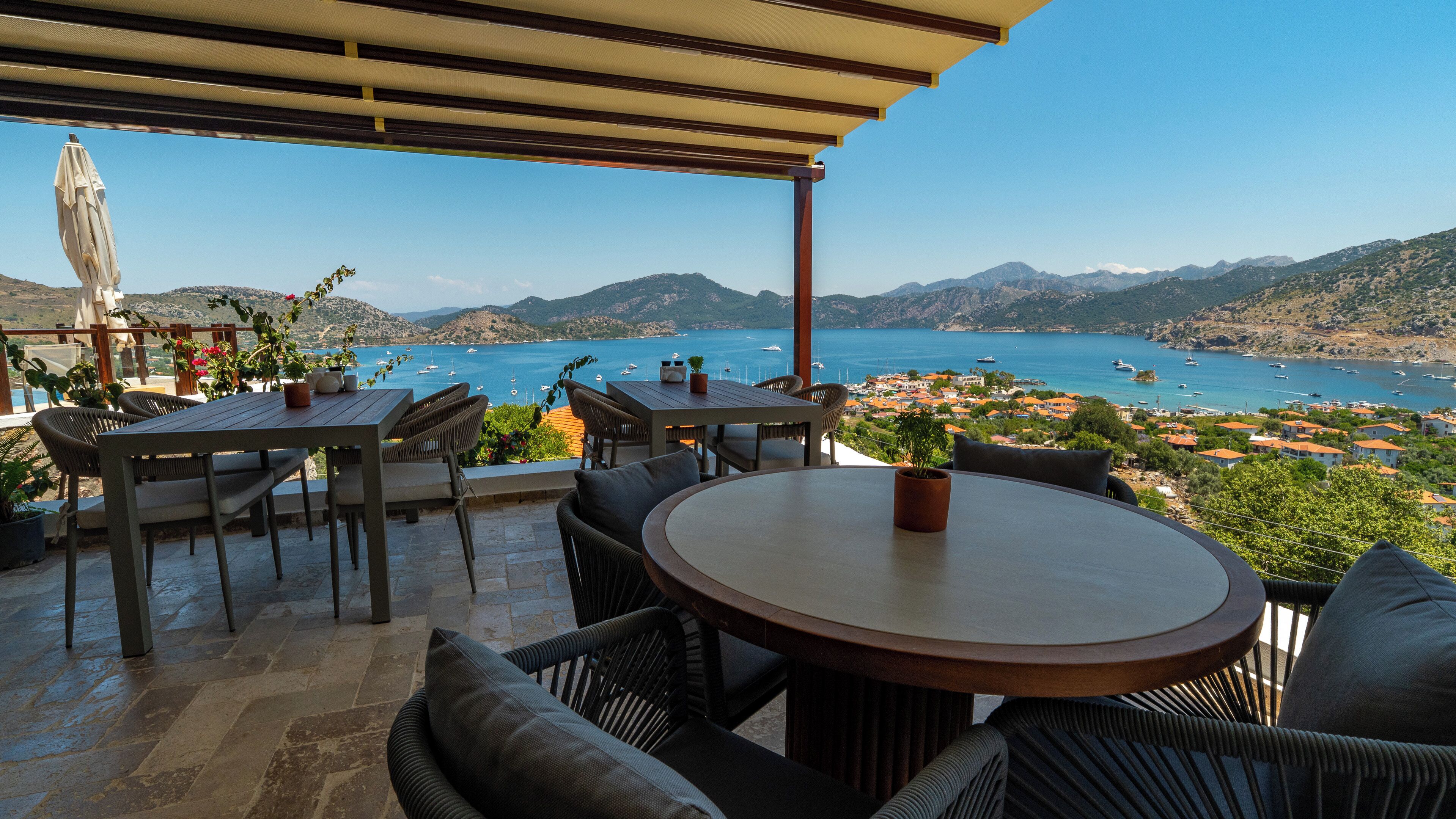 An outdoor patio with tables and chairs, overlooking a coastal town and the sea.