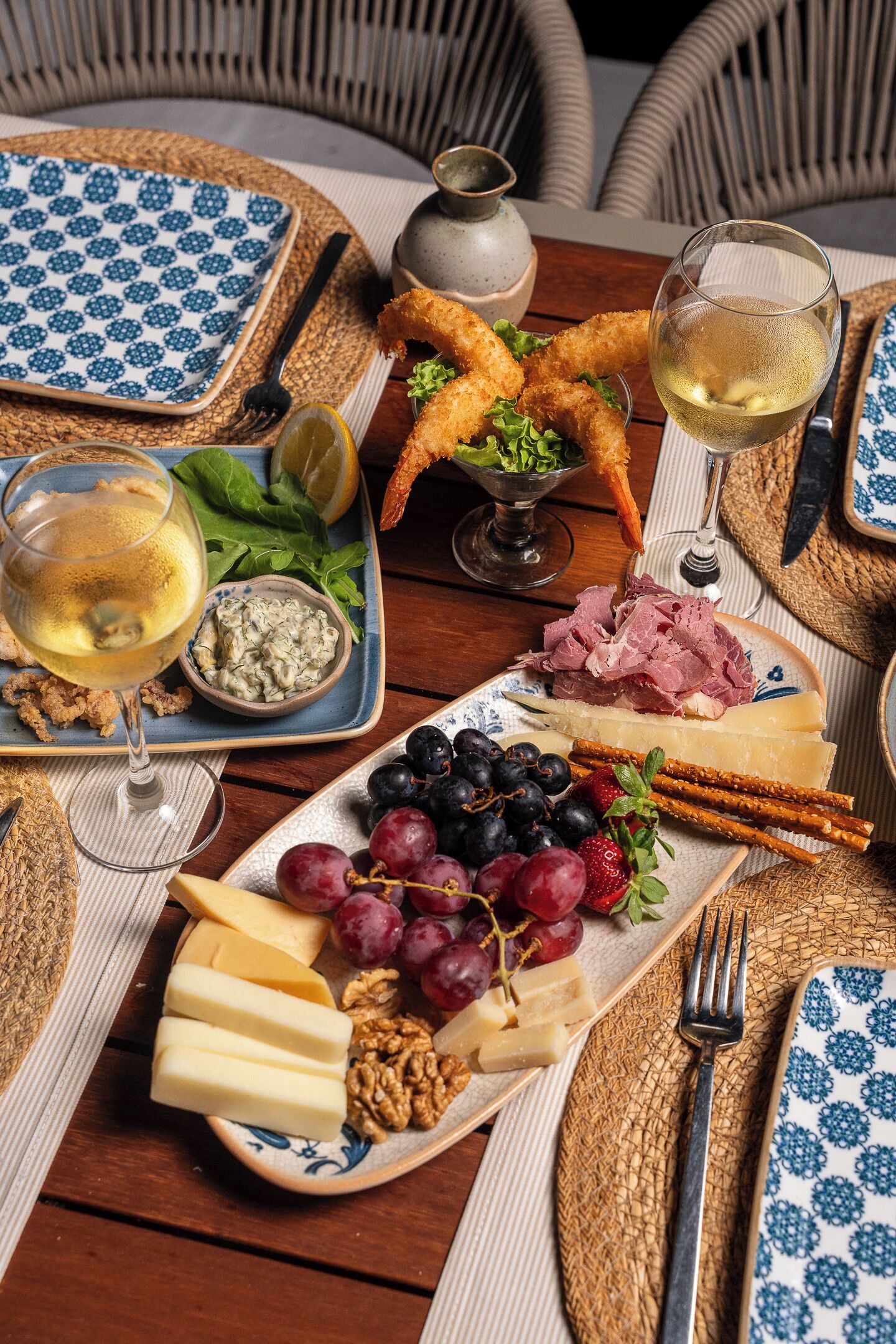 Una mesa servida con diversos alimentos, como queso, uvas, nueces y una copa de vino blanco.