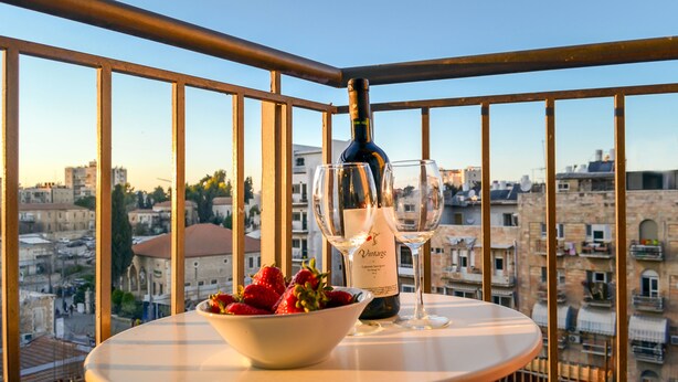 Un balcón con una mesa, una botella de vino y un bol de fresas.