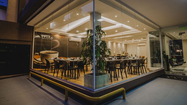 Un moderno vestíbulo de hotel con un amplio ventanal, una planta central y una zona de comedor con mesas y sillas.