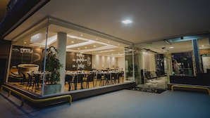 Un restaurante moderno con fachada de vidrio, iluminación interior y un área de comedor con mesas y sillas.