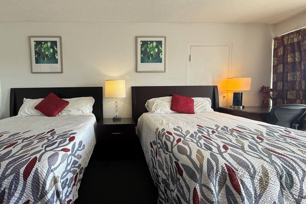 Ein Hotelzimmer mit zwei Betten, jeweils mit einem roten Kissen, einem Nachttisch mit einer Lampe und gerahmten Bildern an der Wand.