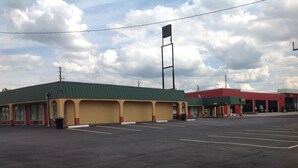 A parking lot with a building that has multiple garage doors and a green roof. - Budget Inn (McDonough)