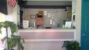 A reception desk with a 'BUDGET INN' sign, a clock, and various informational notices. - Budget Inn (McDonough)
