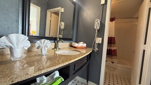 A bathroom with a granite countertop, a sink, a mirror, a towel rack, and a shower area. - Budget Inn (McDonough)
