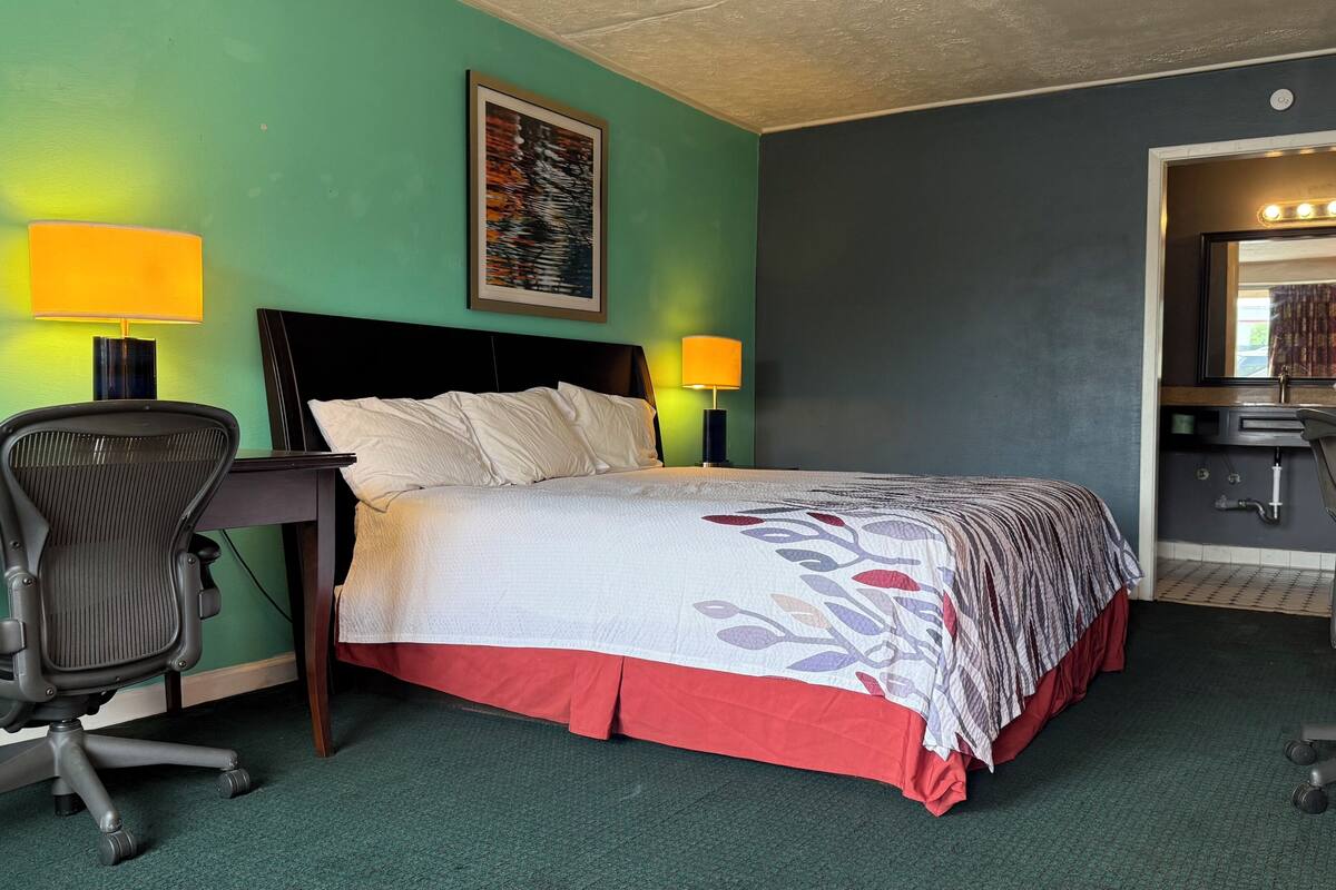 Ein Hotelzimmer mit Bett, Schreibtisch, Stuhl und Spiegel.