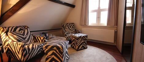 Une pièce de style « loft », avec un plafond haut, des poutres apparentes, une grande fenêtre avec des rideaux et un coin salon confortable agrémenté de meubles à motifs zébrés.