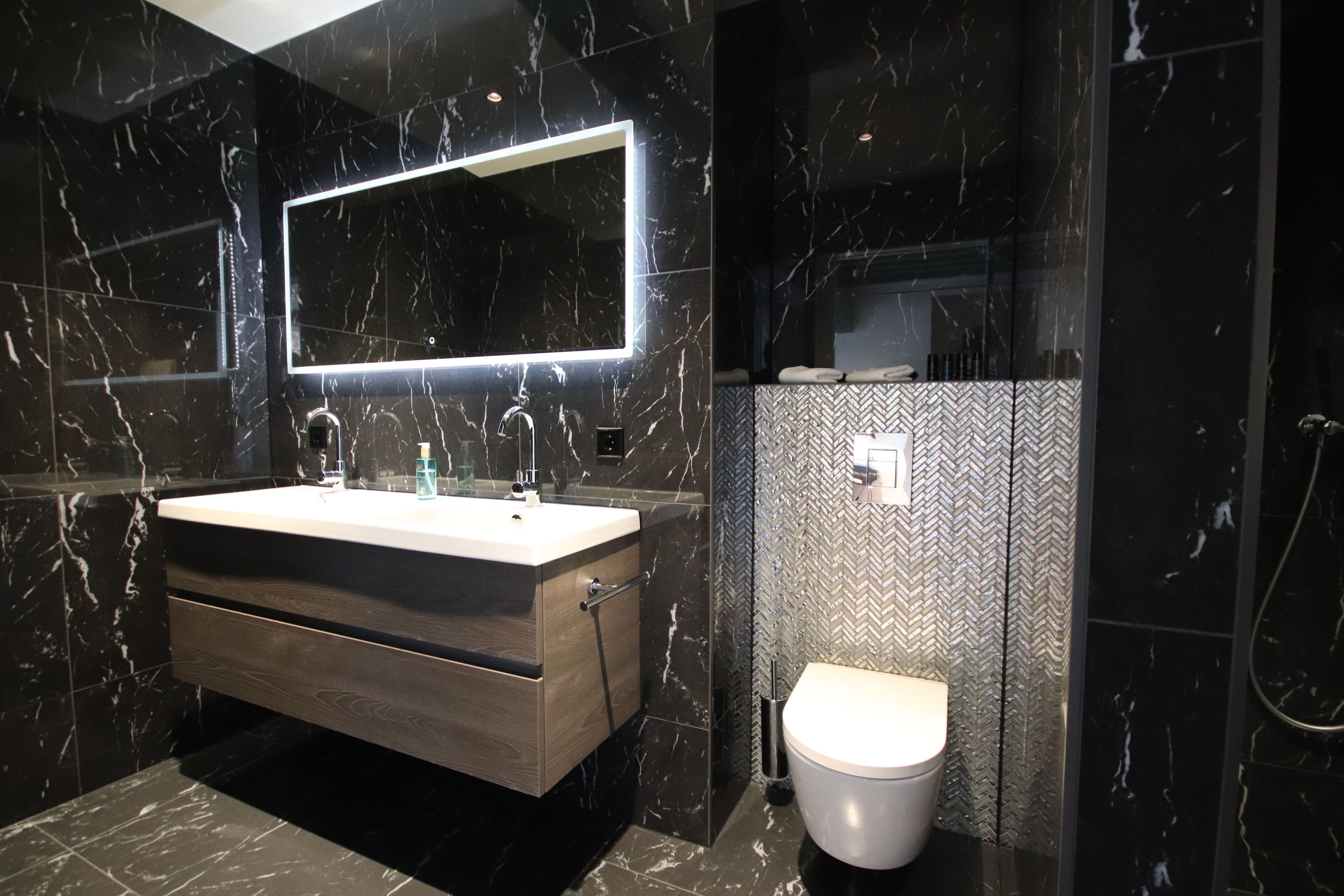 Un baño moderno con tocador de mármol, un espejo grande y pared con motivo de espiga.