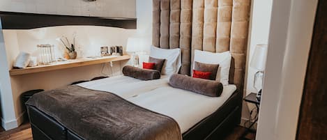 A modern hotel room with a large bed, a bedside table, and a wall-mounted shelf.