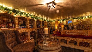 Un rústico área de bar con barriles de madera, sillones de cuero y una variedad de botellas.