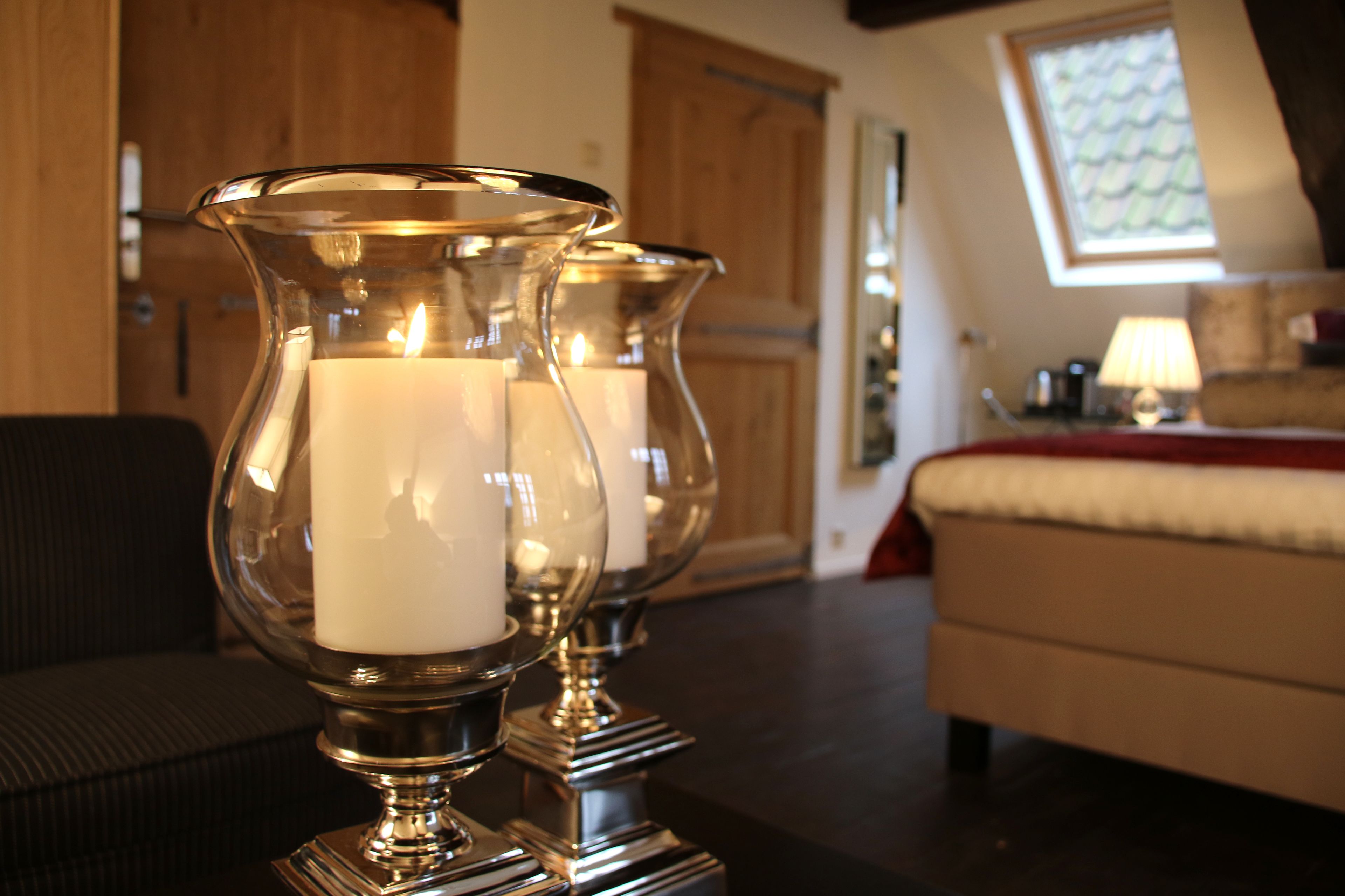A room with a bed, a lamp, and two candle holders with lit candles.