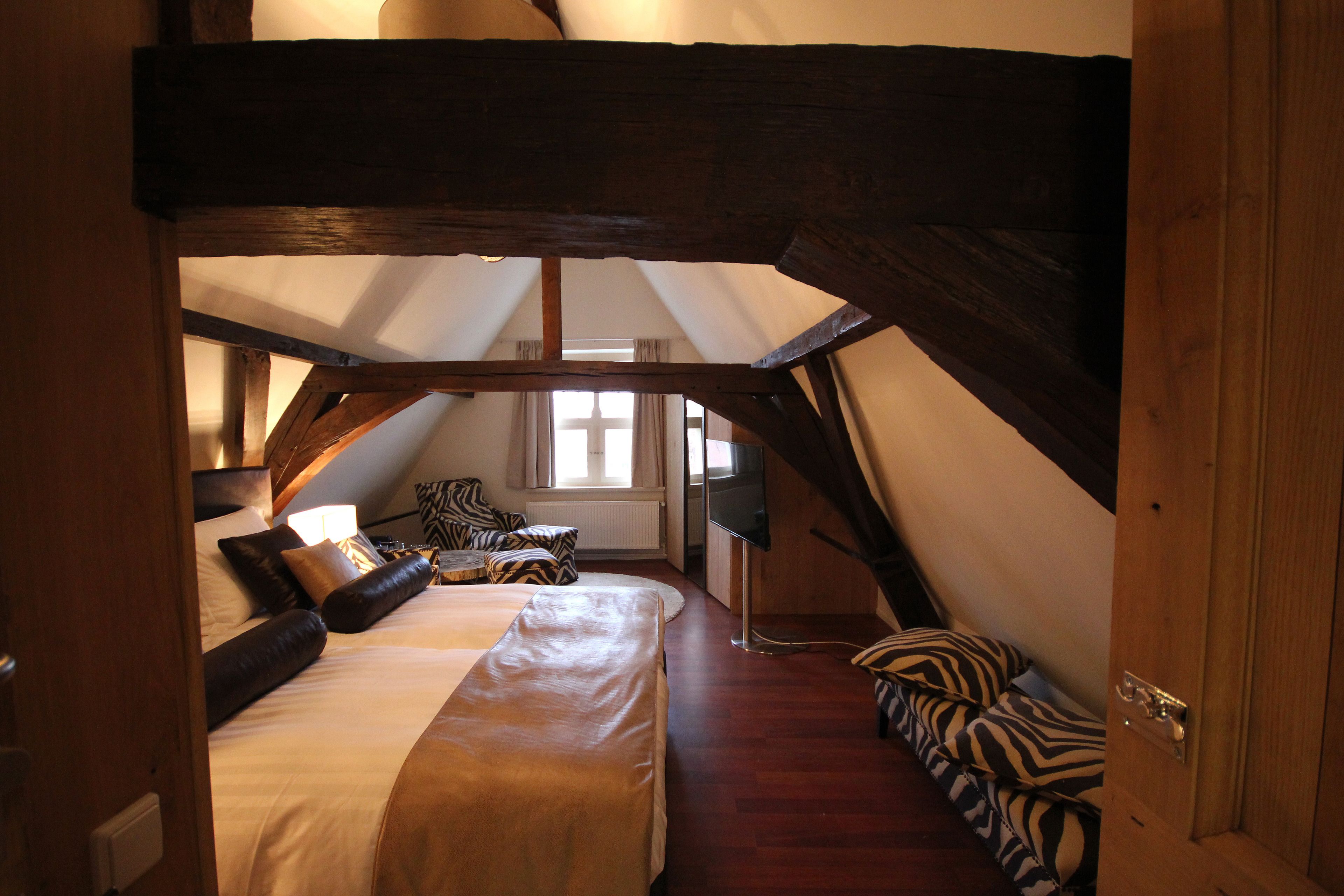 A bedroom with a large bed, wooden beams, and a window.