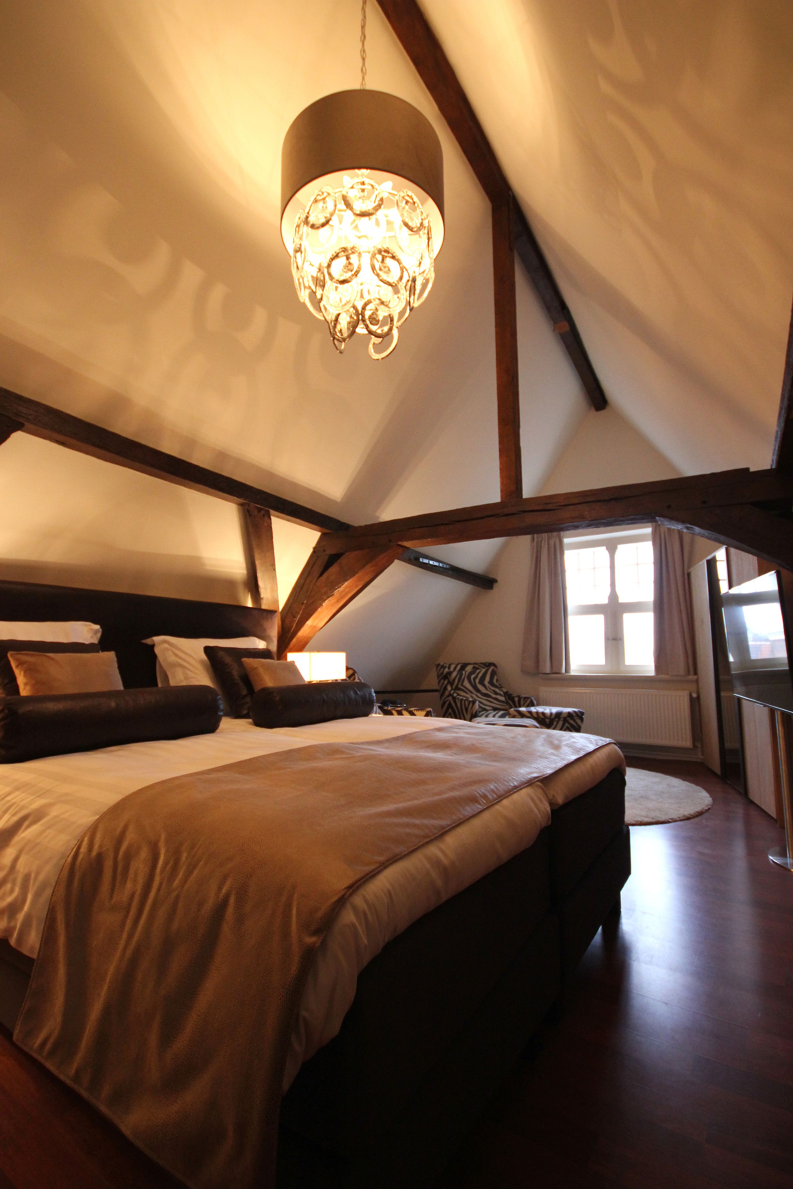 Une chambre à coucher avec un grand lit, un lustre, des poutres en bois, une fenêtre avec des rideaux et une vue sur l’extérieur.