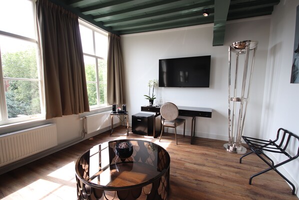 A modern living room with a glass coffee table, a black sofa, a TV mounted on the wall, and a tall floor lamp.