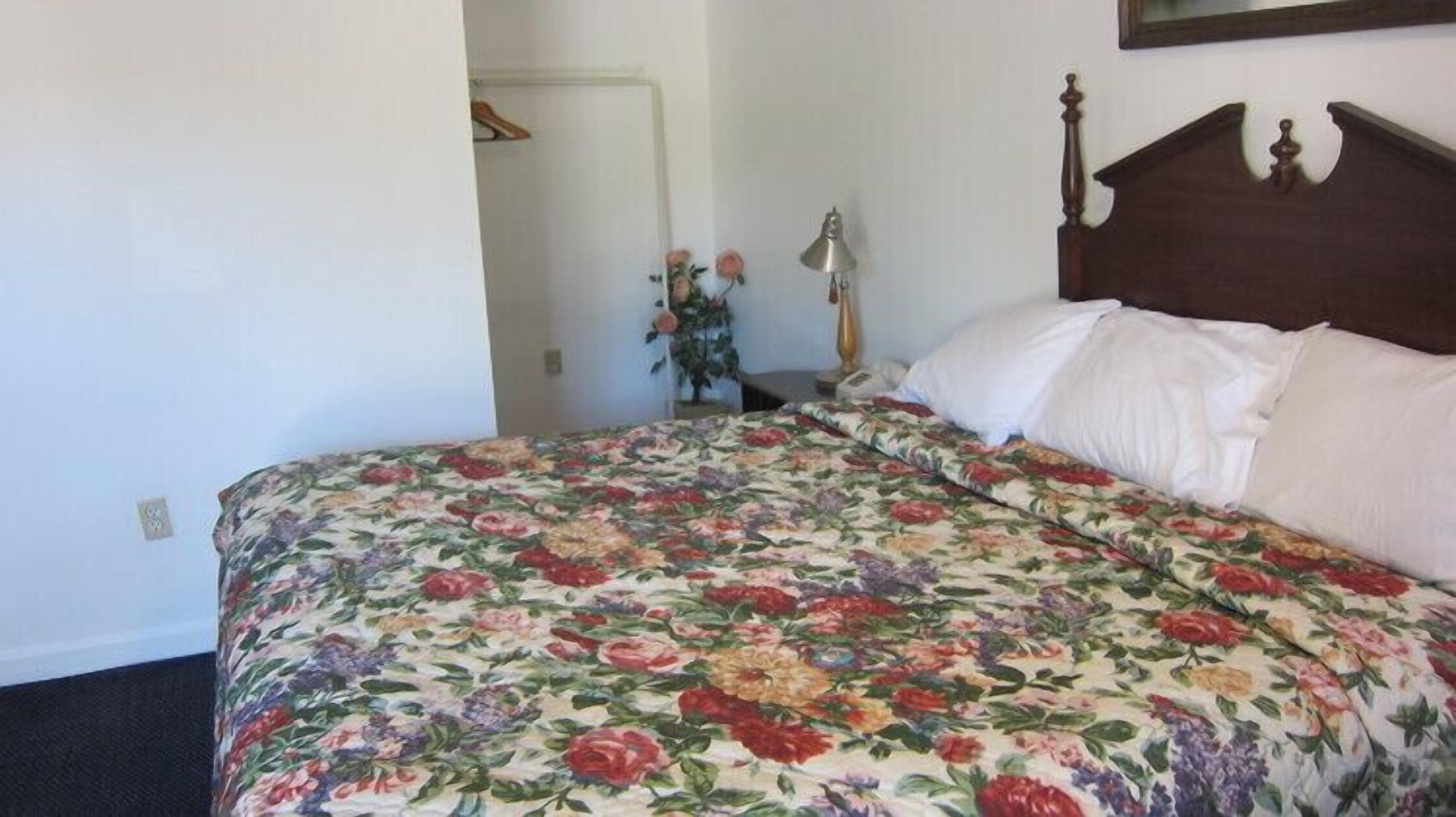 A bedroom with a floral bedspread, a wooden headboard, a bedside lamp, and a door leading to another room.