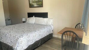 A hotel room with a bed, a small table, a chair, a painting on the wall, and a window with a curtain. - Lamplighter Motel - Clinton, Connecticut (Clinton)