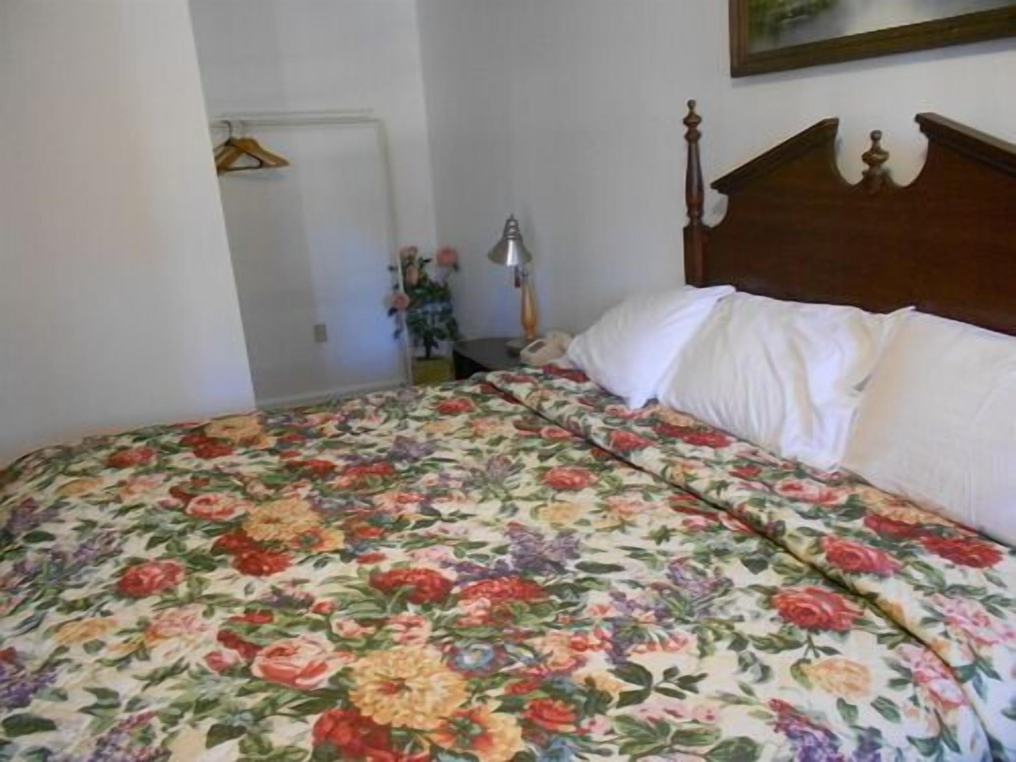 A bedroom with a floral bedspread, a wooden headboard, and a white wall.