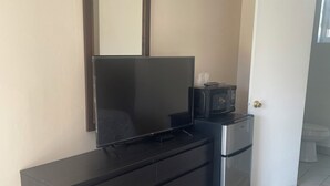 A bedroom with a dark wooden dresser, a flat-screen TV, a microwave, and a door leading to another room. - Lamplighter Motel - Clinton, Connecticut (Clinton)