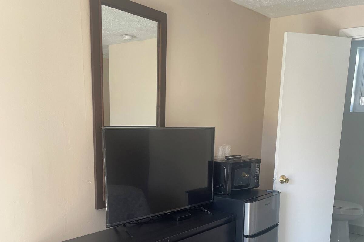 Un dormitorio con un aparador de madera oscura, un televisor de pantalla plana, un microondas y una puerta que da a otra habitación.